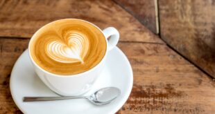 Close up white coffee cup with heart shape latte art on wood tab